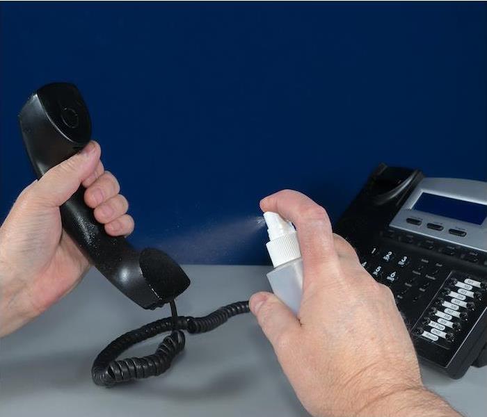 hands spraying a liquid on a black office phone