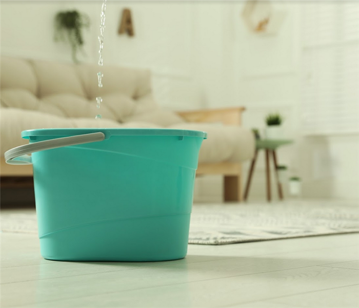 a blue bucket on the floor of a living room catching water that is leaking from the ceiling