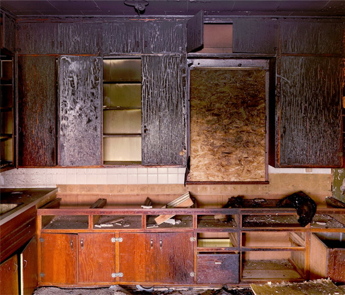 a fire damaged kitchen with debris everywhere and soot covering the cabinets
